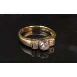 A gold ring with central round cut diamond flanked by diamond baguettes, stamped 750. Size J/K, 3.