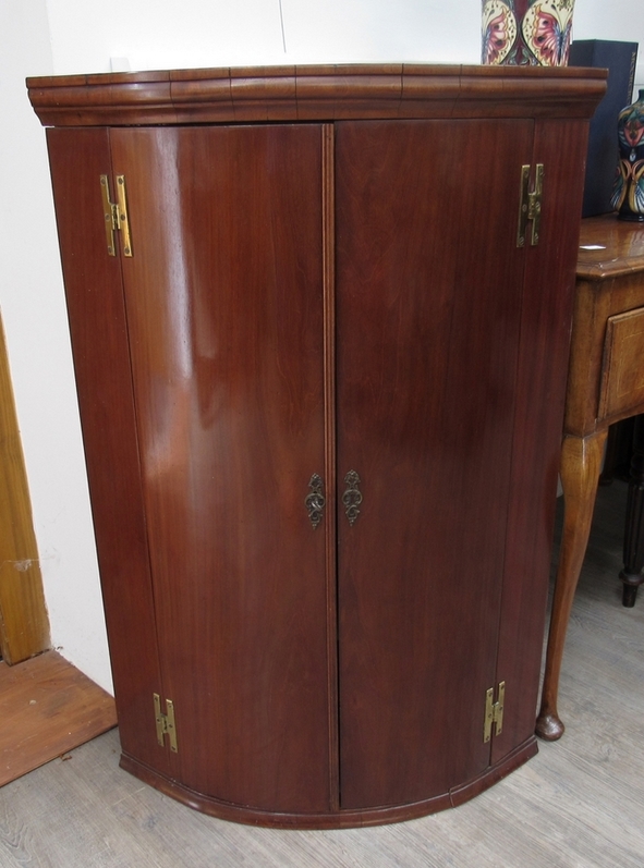 A George III mahogany bow-front wall-hanging corner cupboard with shaped shelves enclosed by a pair