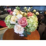 A vase containing faux flowers including roses and hydrangeas