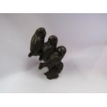 A solid bronze of three baby barn owls perched on a branch,