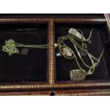 A leather bound jewellery box containing three necklaces with pendants and tie pins