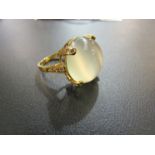 A gold ring set with a large cabochon moonstone, the four claws and shoulders diamond set,
