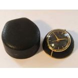 GUBELIN: a gilt metal and leather 8 day travelling alarm clock with black dial and date aperture,