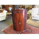 A George III mahogany bow-front wall-hanging corner cupboard with shell patere inlay,
