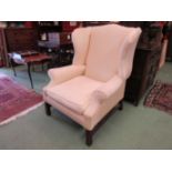 A cream upholstered wingback armchair on stretcher base,
