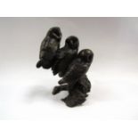 A solid bronze of three baby barn owls perched on a branch,