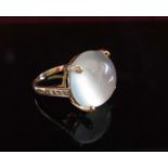 A gold ring set with a large cabochon moonstone, the four claws and shoulders diamond set,