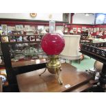 A brass oil lamp on tripod feet with red shade,