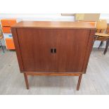 A Danish teak cabinet with tambour front, shelf to interior, raised on square legs.