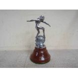 A chromed mascot of a maiden riding a winged unicycle mounted on a turned plinth