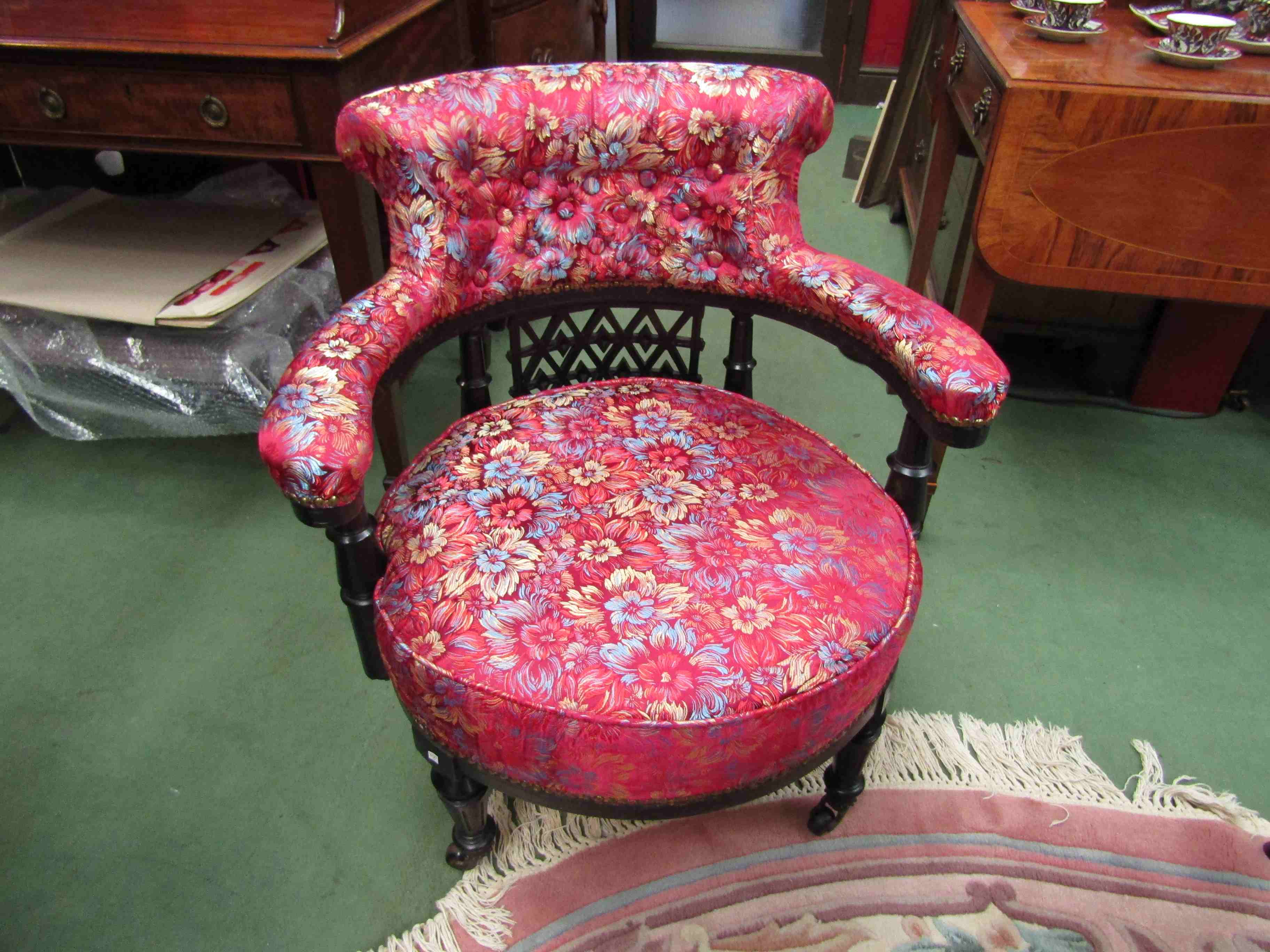 A Victorian ebonised tub chair with floral upholstery on castors