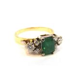An enamelled and diamond ring, the central emerald 7mm x 5mm flanked by diamonds, stamped 750,