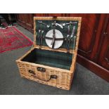 A wicker picnic basket containing plates, cutlery etc.