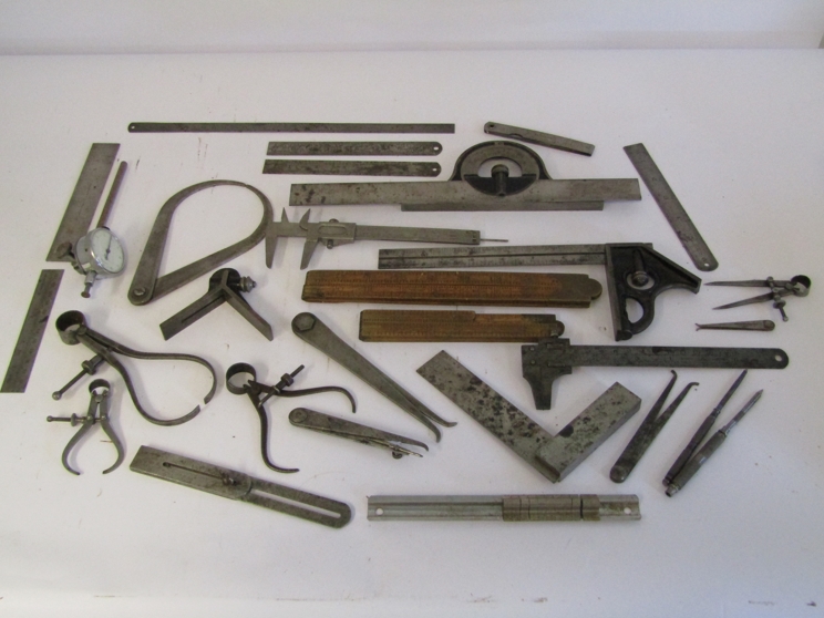 A box of measuring and marking tools including wooden and steel rukes, scribers, squares, calipers,