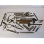A box of measuring and marking tools including wooden and steel rukes, scribers, squares, calipers,