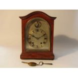 An early 20th Century oak mantel clock with silvered arched dial and Roman chapter ring and