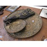 Three embossed brass chargers and two horse brasses on leather