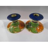 A pair of Clarice Cliff candlesticks in the "Orange Lily" pattern, both hairlined and chipped,