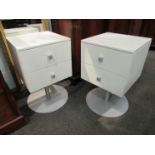 A pair of white two drawer revolving chests on circular metal bases,