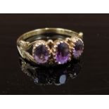 A 9ct gold ring with three oval amethysts, ornately patterned shoulders. Size S/T, 2.