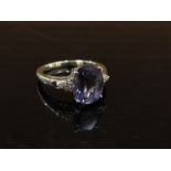 A 9ct white gold ring with oval purple stone flanked by diamond set shoulders. Size R, 3.