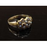 A gold ring with two linked seed pearl seed pearl flowers set with a diamond and ruby centre,