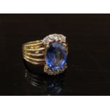 A gold ring with oval synthetic sapphire in multi split shoulders, stamped 9ct.