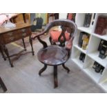 A Victorian mahogany revolving desk chair the scroll end arms over a saddle seat and castors