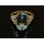 A gold ring set with large oval pale blue stone, 13mm x 9mm flanked by diamond set split shoulders,