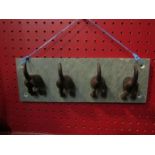 A slate rack of four metal hooks in the form of dogs tails,