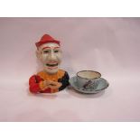 A cast metal clown money box and child's enamel cup and saucer