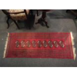 A red runner rug with multiple borders and gulls with tasselled ends,