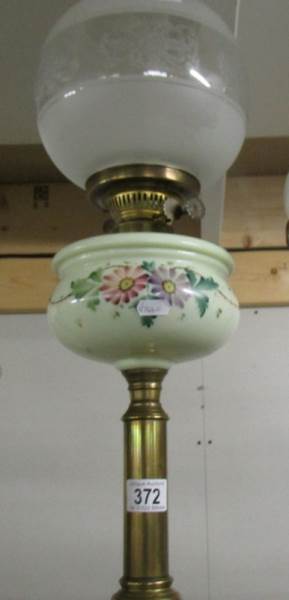 A brass oil lamp with floral decorated front and complete with shade and chimney.