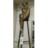 A heavy metal figure of a nude sat on a high stool.