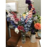 A vase and jug containing artificial flowers
