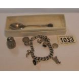 A silver charm bracelet with charms including silver, a silver teaspoon and a thimble,
