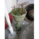 A stone urn planter on a raised stone pedestal