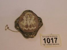 A large shell cameo brooch depicting 'The Three Graces' in yellow metal mount with safety chain.
