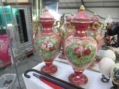 A pair of large early 20th century pink and gilded floral decorated lidded urns