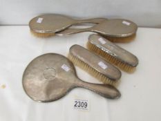 4 hall marked silver backed hair brushed and a silver backed hand mirror.