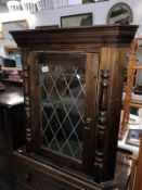 A dark stained pine corner cupboard with leaded glass door