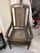 An Edwardian oak commode chair with bergere panels.