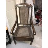 An Edwardian oak commode chair with bergere panels.