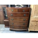 A mahogany veneered bow front chest of drawers with brass handles.