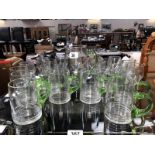 A large quantity of drinking glasses and a jug with green handles.