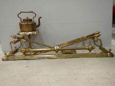 A Victorian brass fender, set of brass fire irons, brass trivet and copper kettle.