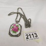 A porcelain pendant by Jan Gemalt in silver depicting roses in a fancy cutwork mount attached to a