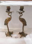 A pair of brass candlesticks in the form or heron/stork standing on a tortoise whilst holding a