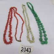 A green jade bead necklace, a white jade bead necklace and a coral necklace.