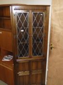 A drak oak corner cupboard with leaded glass doors